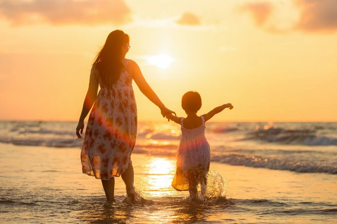 Madre e hija caminando de la mano en la playa al atardecer